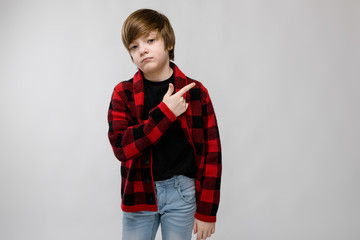 Cute confident serious little caucasian boy in checkered shirt showing on blank area on grey background