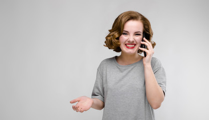 Charming young girl in a gray T-shirt on a gray background. The girl speaks by phone