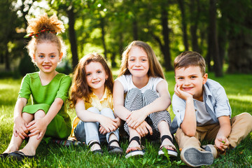 A group of children of school and preschool age are sitting on the green grass in the park.
