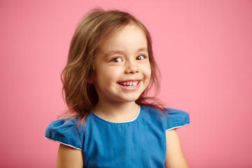 beautiful surprised child girl with cute smile and sincere look, is in a good mood, expresses joy and happiness, close up kid portrait on pink background.