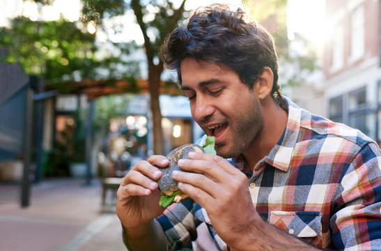 Smiling Young Man Sitting Outside Eating A Delicious Bagel