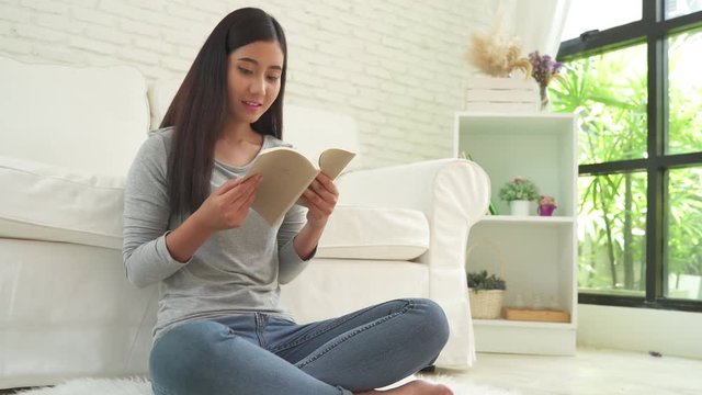 Beautiful asian woman enjoying time and sitting on modern sofa in front of window relaxing in her living room reading book. lifestyle asia woman at home concept.