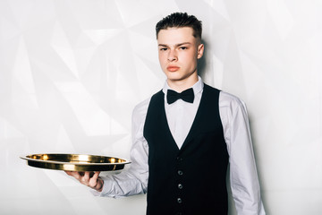 Portrait of male waiter who is holding tray in hall of restaurant.Portrait of waiter with serving...