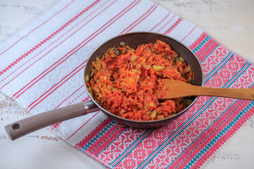 Stewed vegetables on a skorodka on a table. Carrots, tomato, onions.