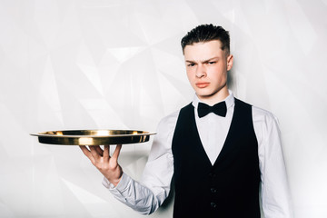 Portrait of male waiter who is holding tray in hall of restaurant.Portrait of waiter with serving...