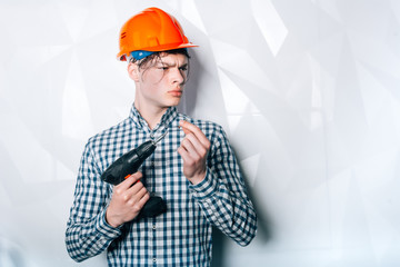 A man in helmet with a screwdriver.Stroitel, designer, designer, architect. Repair in the apartment. Services.Attractive young man in an orange construction helmet