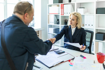 A young girl is sitting at a table in the office. The girl shakes hands with the man.