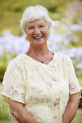 Portrait Of Senior Woman Enjoying Walk By Flower Beds In Park