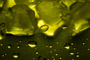 Ice cubes in lemon color on a reflecting table with drops of water