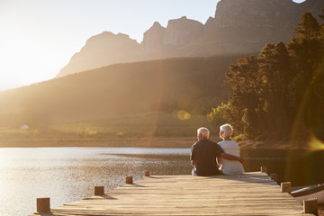 Romantic Senior Couple Sitting On Wooden Jetty By Lake - Powered by Adobe