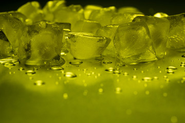Ice cubes in yellow on a reflecting table with ice drops