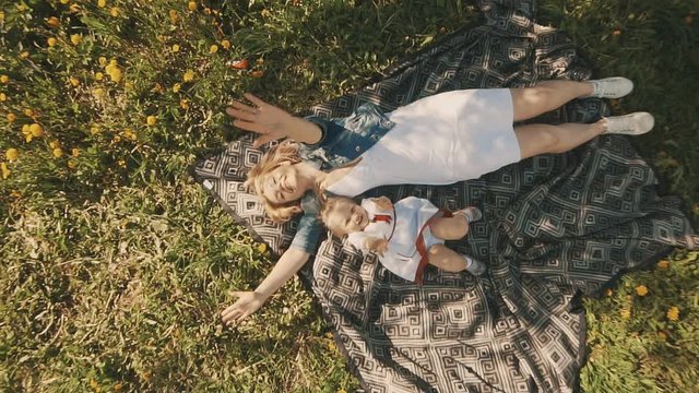 Mother and daughter lying on lawn. Family in city park outdoors. Happiness of motherhood and childhood in slow motion. Top view