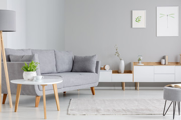 Table next to grey sofa in scandi living room interior with posters above cupboard. Real photo