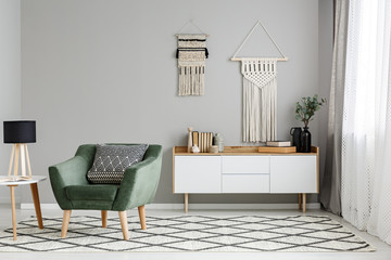 Green armchair on patterned carpet near table with lamp in minimal living room interior. Real photo