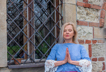 Portrait of beautiful mature woman practicing yoga and meditation,  with her palms together,  outdoor. Namaste. Longevity concept 

