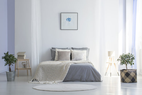 Round rug in front of grey bed with blanket in minimal bedroom interior with poster. Real photo