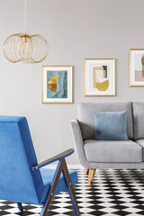 Real photo of a blue armchair standing in front of a grey couch in living room interior with...