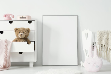 Plush toy in cabinet next to poster with mockup and cradle in baby's bedroom interior. Real photo. Place for your graphic