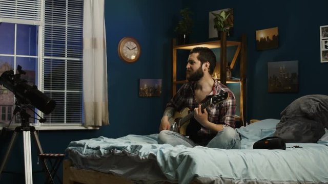 Casual man and girl relaxing on bed at home and having fun with guitar while singing song together