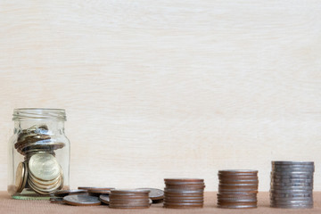 Glass of coin and four pole range of coins on vintage blurred background - Saving money concept.