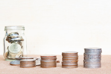 Glass of coin and four pole range of coins on vintage blurred background - Saving money concept.
