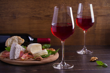 Glasses of wine with cheese, bread, nuts, prosciutto and basil. Wine and food on wooden table. horizontal, room for text