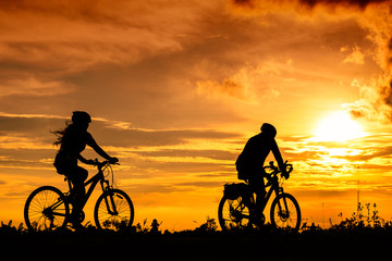 A man and a woman ride bicycles on the road with beautiful colorful sunset sky. Sport and active life concept.