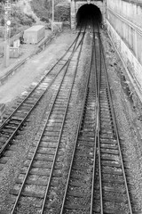 Fototapeta na wymiar Overhead train tracks merging together going into dark tunnel in black and white.