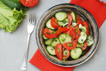 Tomato and cucumber salad vegan food with fork gray textured cement background
