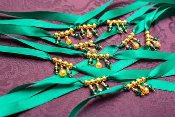 Beautiful sparkling glamorous embellishments on the ribbon, bridesmaids necklaces, emerald and gold color, purple background, party decorations