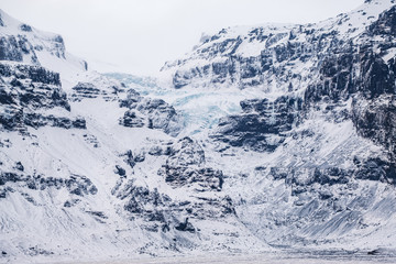Dramatic icelandic landscape with snow covered rocky mountains with frozen glacier and warefalls.