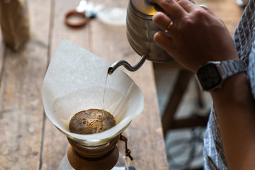 Hand drip coffee, Barista pouring water on coffee ground with filter on wooden table, vintage style