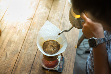 Hand drip coffee, Barista pouring water on coffee ground with filter on wooden table, vintage style