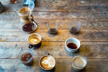 Different cups of coffee on wooden table, top view, vintage style