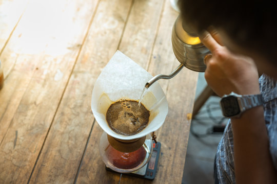Hand drip coffee, Barista pouring water on coffee ground with filter on wooden table, vintage style
