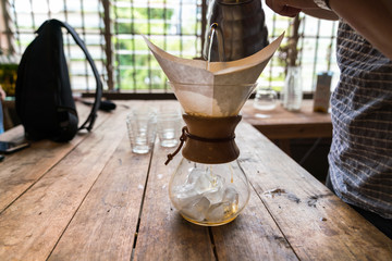 Hand drip coffee, Barista pouring water on coffee ground with filter on wooden table, vintage style