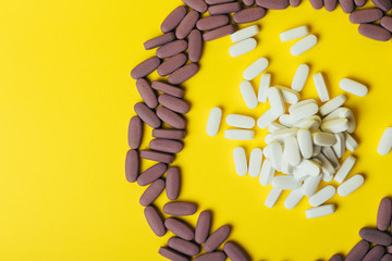 a lot of violet, oval tablets, pills scattered, scattered on a yellow background in the form of a circle, in the middle of the circle are scattered white pills, oval, space for text