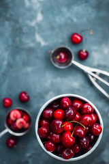 Cherries with an ice cream spoon and metal bucket on a grey concrete background, Summer berries concept with copy space. Neutral color tones still life