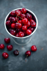 Cherries with a small metal bucket on a grey concrete background, summer berries concept with copy space. Neutral color tones still life