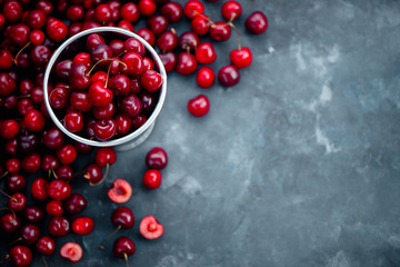 Cherries with a small metal bucket on a grey concrete background, summer berries concept with copy space. Neutral color tones still life