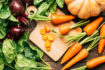 carrots, beets, spinach on a wooden background, cutting board and knife, fresh vegetables