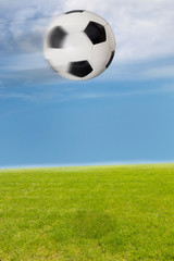 Fliegender Fußball über dem Rasen vor blauem Himmel