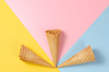 Ice cream waffle cones over light yellow, sweet pink and light blue background with copy space for text, logo or wordings insertion or decoration, colourful summer cold sweet snack concept