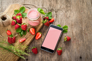 Strawberry smoothies in glass with many strawberries and electronic gadget on wooden background. Top view. Copy space