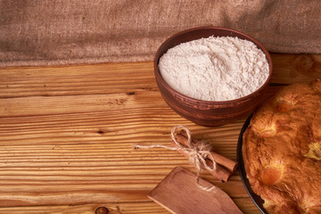 On a dark wooden table, fashionable bakeries, a bowl with flour, apricot cake and tools stand on table