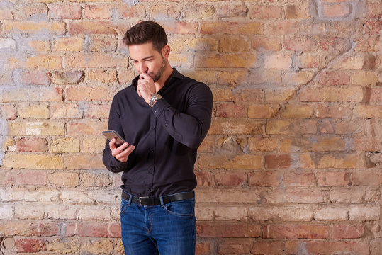 A thinking handsome young businessman using his smartphone in a black shirt.