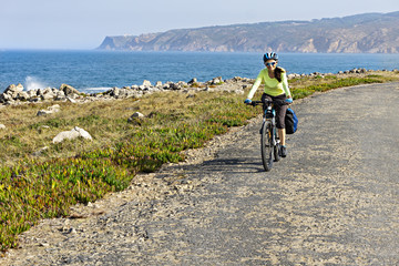 Happy female cyclist  rides a bicycle on the road along the ocean shore  and looking at the camera.