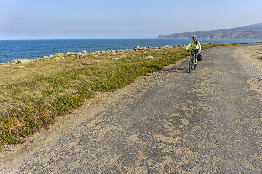 Happy female cyclist  rides a bicycle on the road along the ocean shore  and looking at the camera.