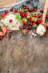 Fresh sweet cherries and strawberries with cottage cheese on wooden background. Top view. Copy space. Flatlay
