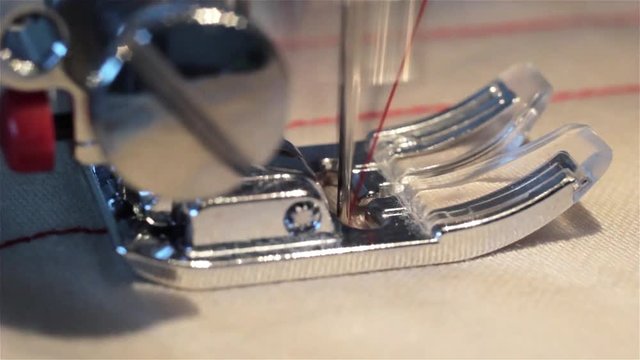 sewing machine close up. Sew Denim Macro. The needle of the sewing machine sews a red thick cloth in slow motion. The thread passes through the fabric.